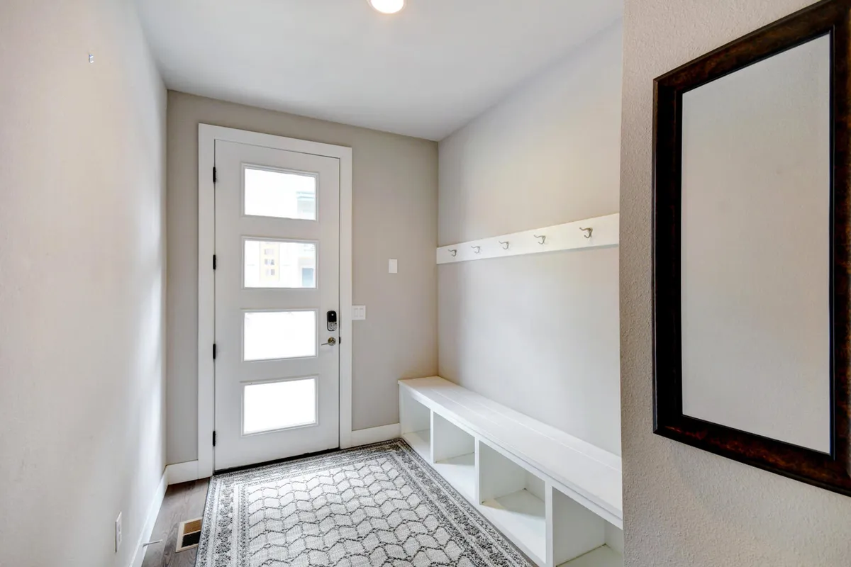 A welcoming entryway with a sturdy front door, a comfortable bench for putting on shoes, convenient wall hooks for gear, a large mirror, and a cozy area rug. The space is thoughtfully arranged for organizing belongings before heading out for adventure or bringing them in after a day outside.
