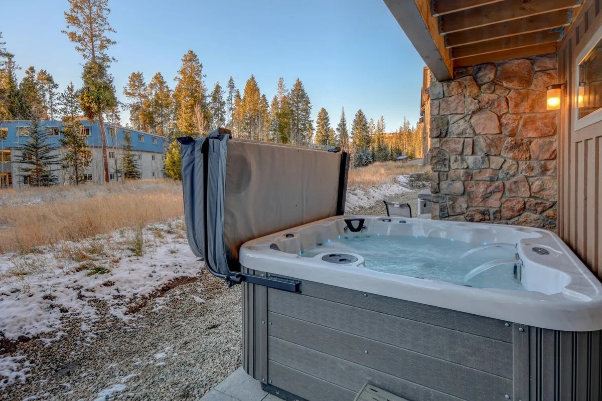 An outdoor hot tub set against natural stonework and surrounded by trees, with the home’s stone wall in the background. The mood is tranquil, capturing the promise of soaking under the stars after a day of excitement.