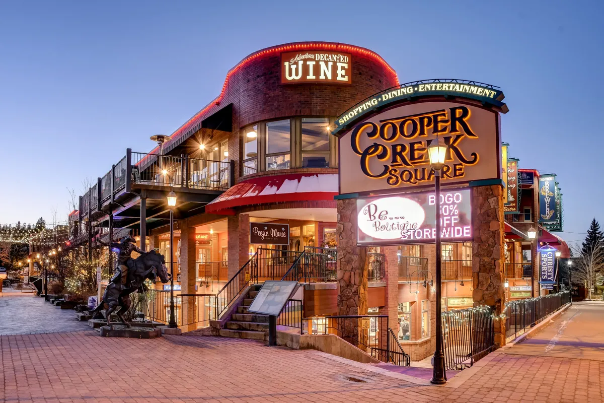 A vibrant exterior shot of Cooper Creek Square, showcasing signage, boutique wine shops, inviting architecture, and lively elements like stairs and sculptures. The scene captures the vibrancy of local dining, shopping, and nightlife, all easily accessible from the home.