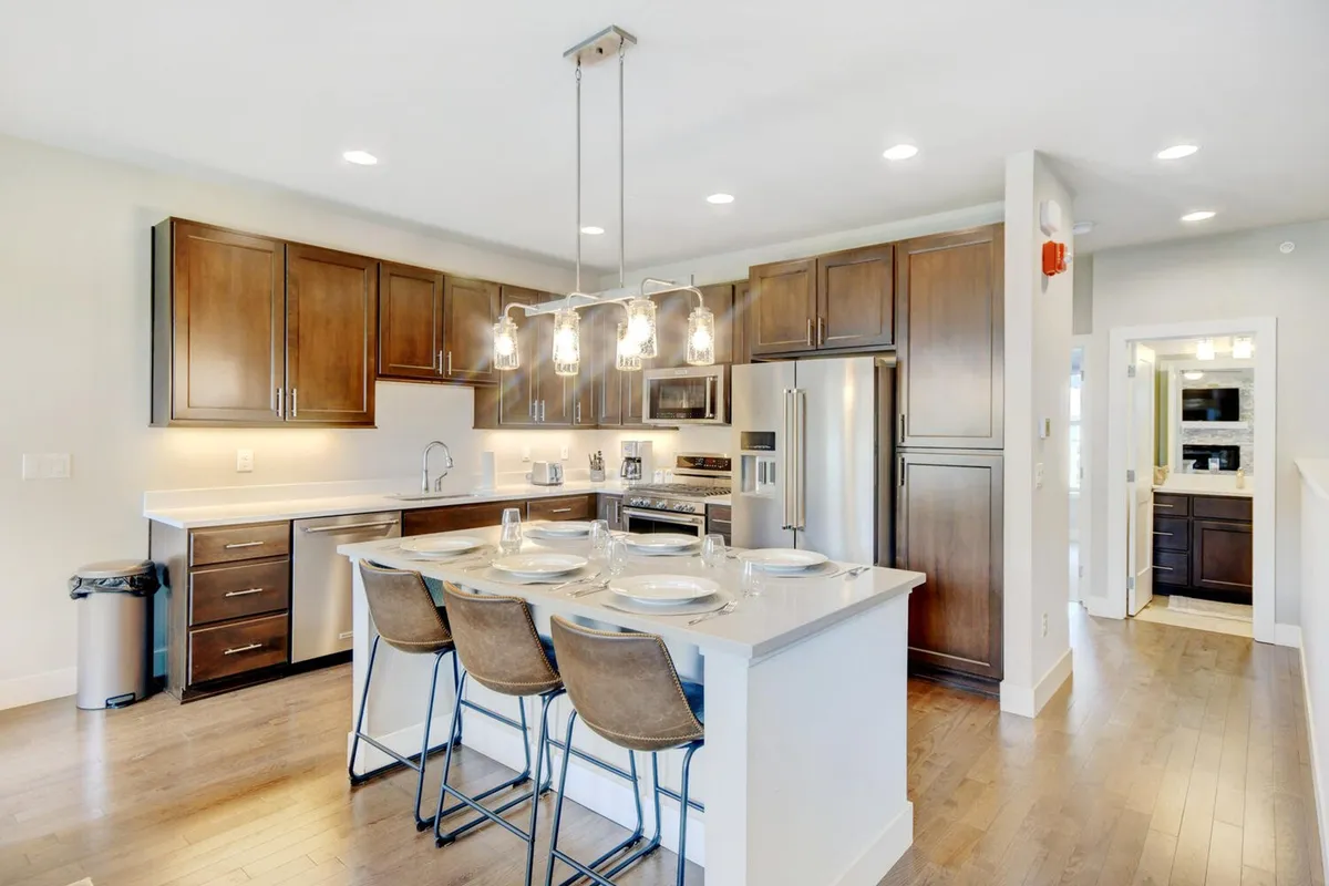 A bright, inviting kitchen interior with a central island countertop, stylish stools, and contemporary lighting. The cabinetry and appliances are modern, and the open layout encourages group cooking, entertaining, or casual family dining. The space feels accessible and family-friendly, echoing the section's emphasis on effortless and inclusive meals.