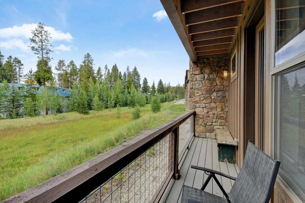 A peaceful exterior balcony scene with a comfortable seating area framed by sleek railing. Lush greenery and distant trees provide a private, natural backdrop perfect for quiet relaxation or soaking up the sunrise. The atmosphere is serene and exclusive.