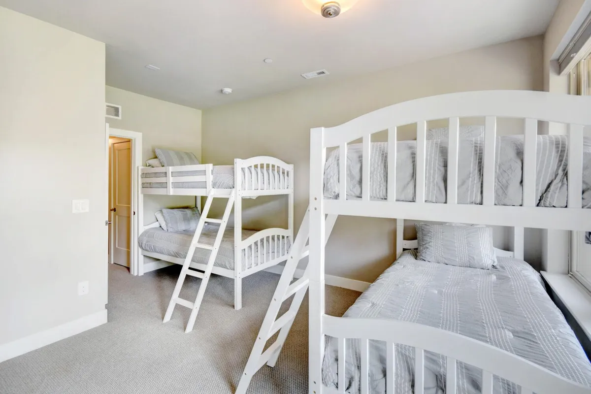 A cozy bunk room with textured bedding on twin bunks, a window letting in natural light, and playful touches that invite children to read, play, and relax together.
