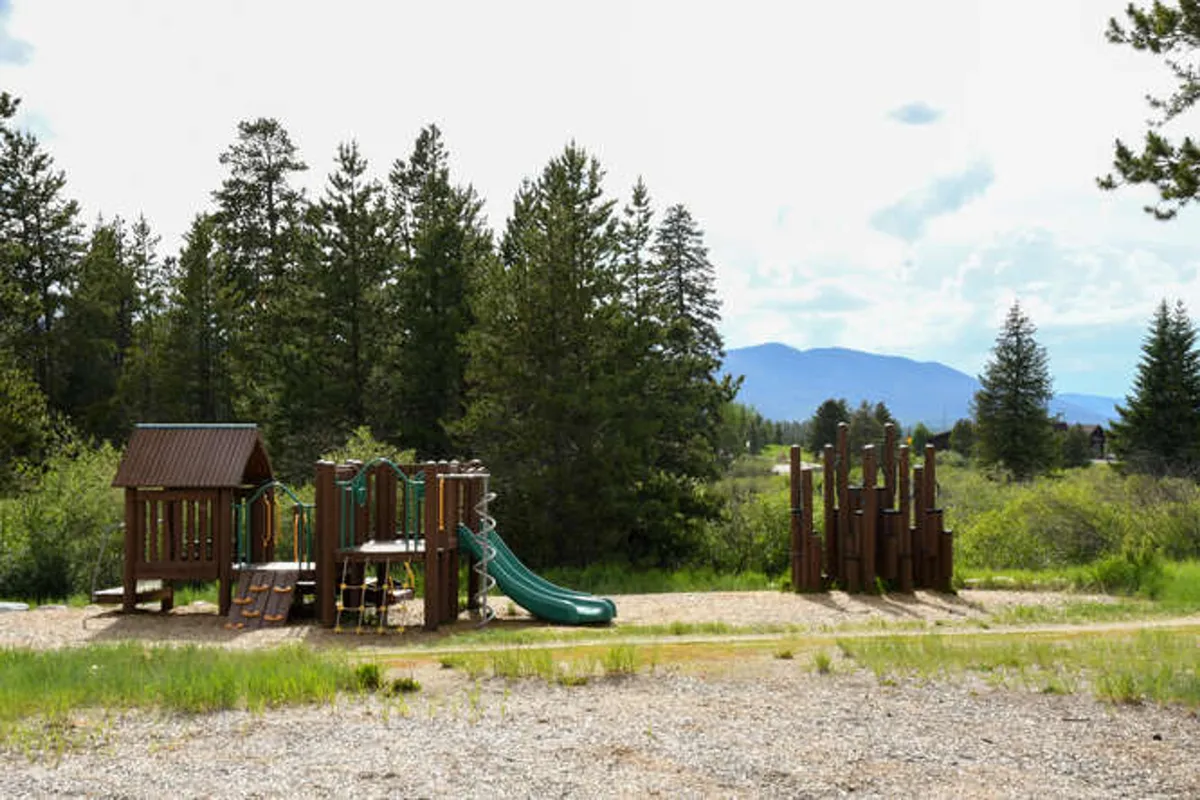An active playground structure surrounded by trees, with children playing, invites families to enjoy outdoor spaces. The natural setting and open area also create a pet-friendly atmosphere for walks and play.