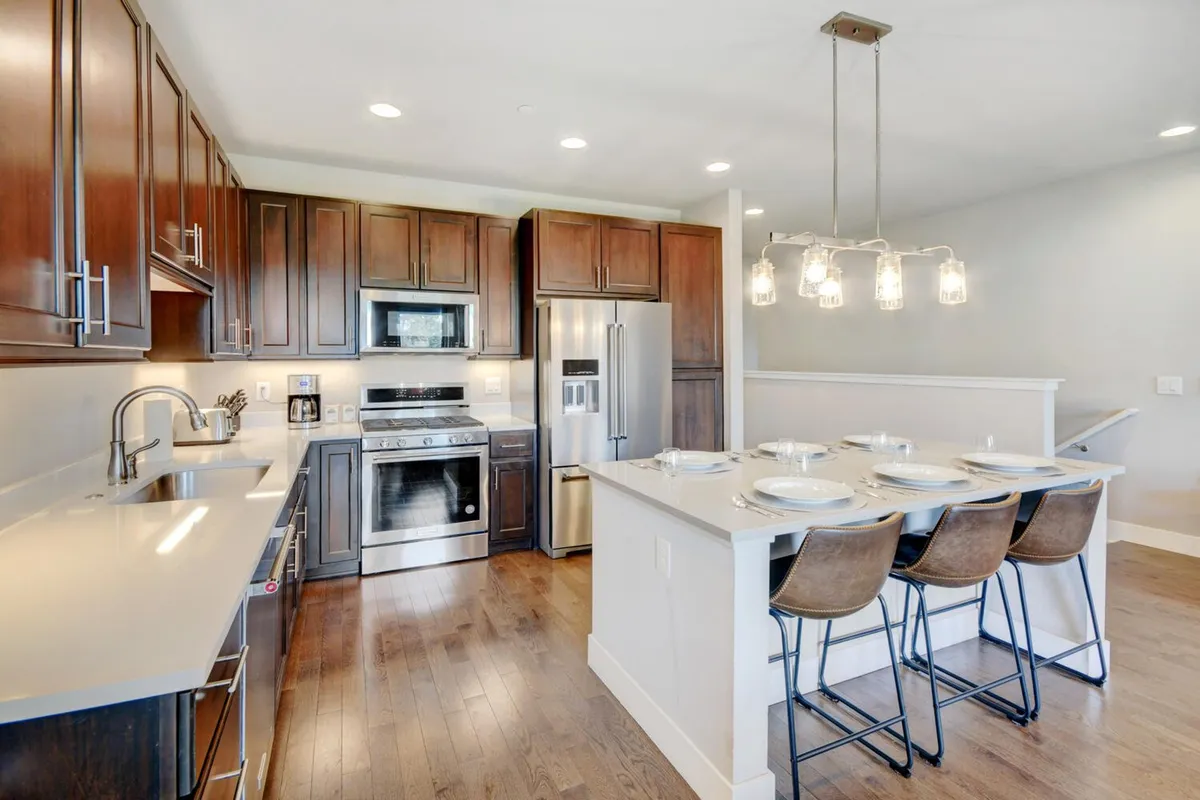 A warmly lit, modern kitchen featuring a large island with bar stools, sleek appliances, and pendant lighting. The space is open and inviting, perfect for both preparing meals and gathering with friends or family. The visible counter space and seating showcase functionality for family breakfasts, casual snacks, or celebrations.