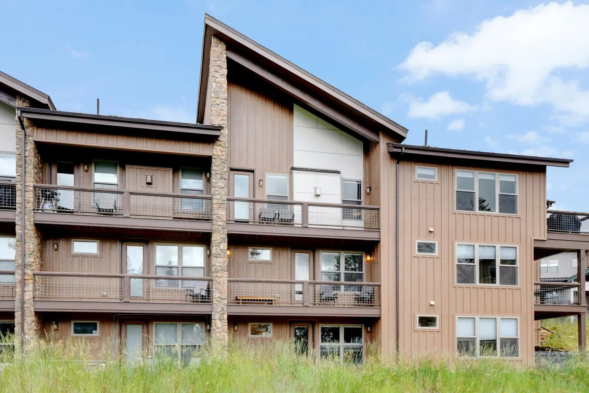 An inviting exterior shot of a luxury building featuring multiple balconies, a striking stone facade, and expansive windows. The image highlights spaces for relaxing outdoors, enjoying sunset views, or gathering with loved ones, all set against a backdrop of natural beauty.
