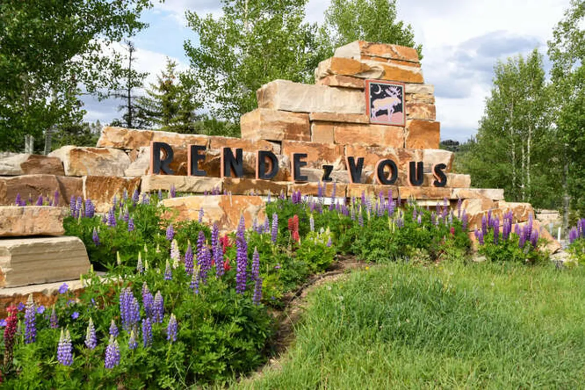 This exterior image features a welcoming rock formation with clear signage and vibrant flower beds in the foreground. The area is surrounded by nature, suggesting easy access to trails and outdoor spaces perfect for walking dogs.