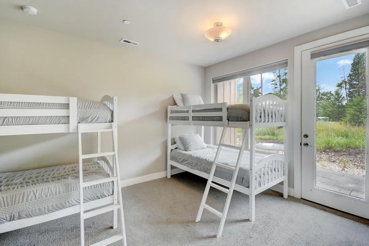 A playful bunk room featuring sturdy twin bunk beds, large windows letting in daylight, and an inviting view of the outdoors. The space feels bright and lively—ideal for children or friends to enjoy a fun sleepover atmosphere.