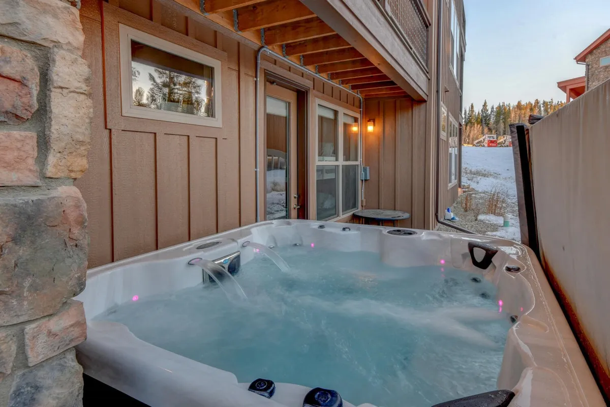 A beautiful exterior view of a hot tub next to the stone wall of the home, with windows reflecting the golden hour light. The space feels private, inviting, and perfect for enjoying evenings.